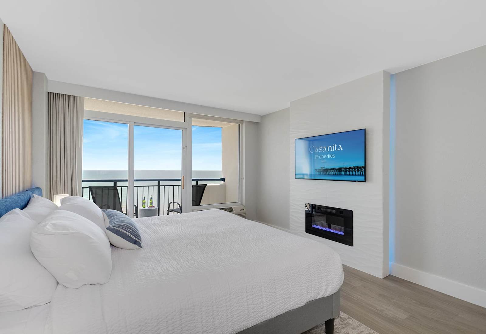 Wake up to serene ocean views in this stylish bedroom with floor-to-ceiling windows and a private balcony. Enjoy natural light, a cozy bed, modern fireplace, and sleek TV, blending comfort and luxury. Perfect for a relaxing retreat by the sea.