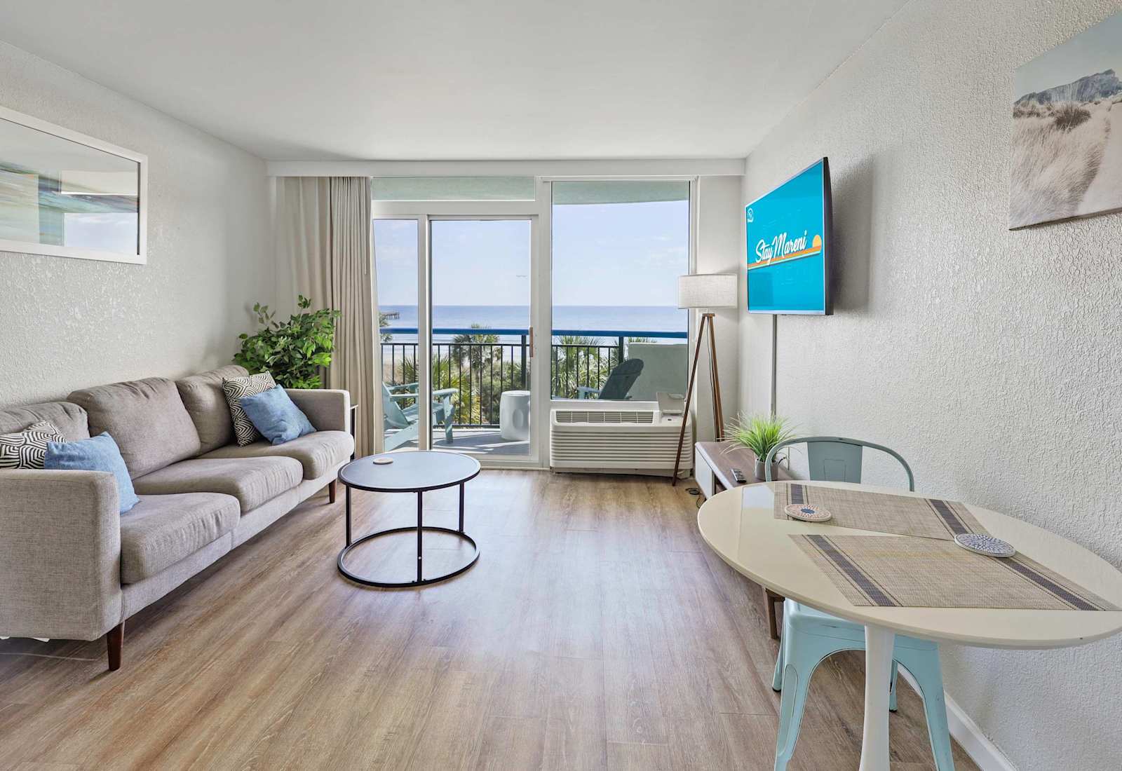 Bright, coastal-inspired living space with modern furnishings, a cozy seating area, and a private balcony showcasing stunning oceanfront views.