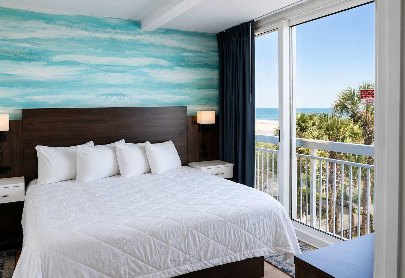 Rest easy in this bright, airy bedroom featuring a serene coastal accent wall and direct balcony access!