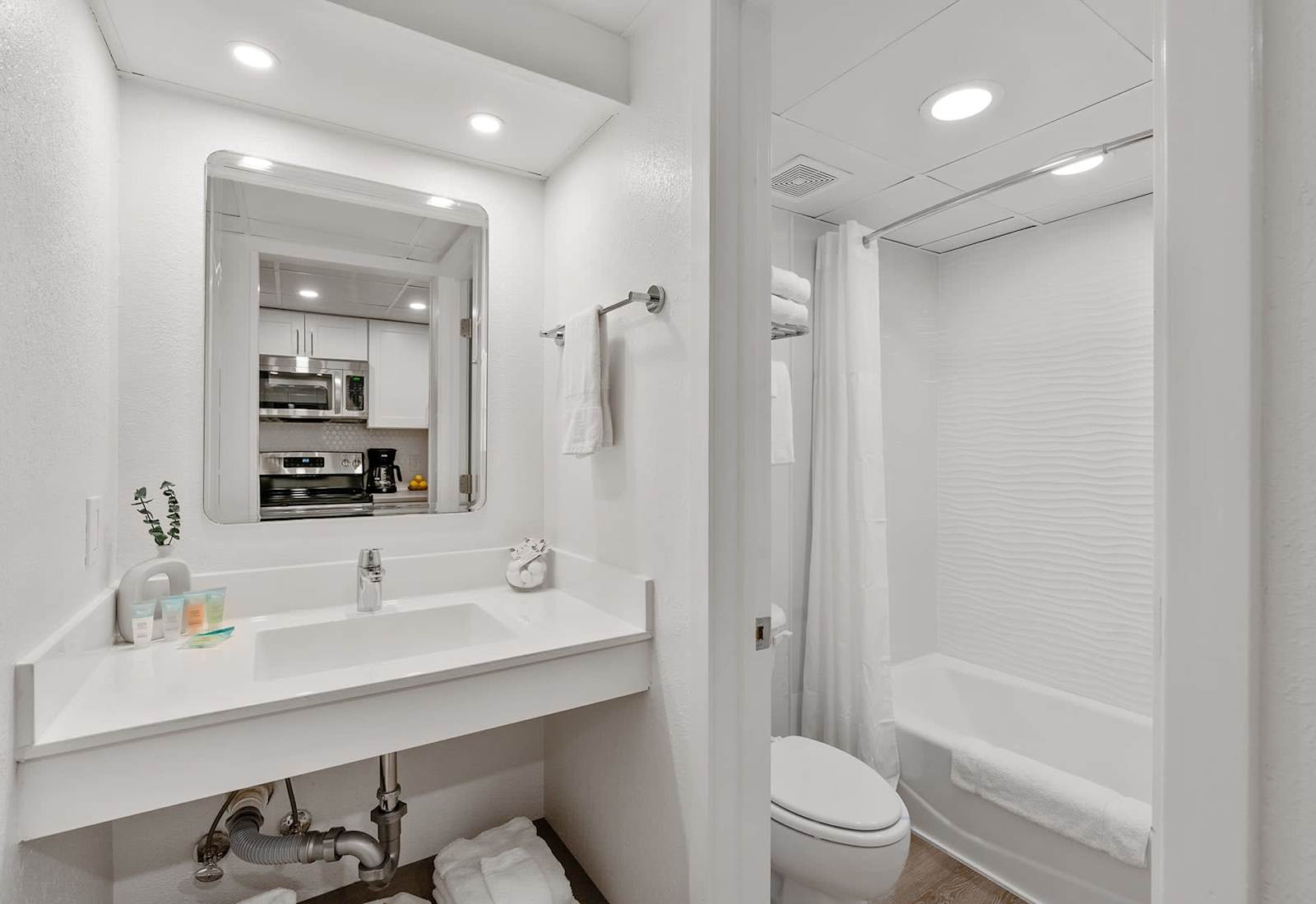 A bright, modern bathroom with crisp white tiles, a relaxing bathtub, and plush towels awaits your stay! 
