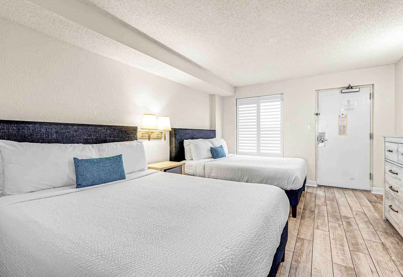 Rest easy in this bright, coastal-inspired bedroom featuring two plush queen beds, crisp linens, and calming tones—perfect for families or friends looking to unwind after a fun day at the beach.
