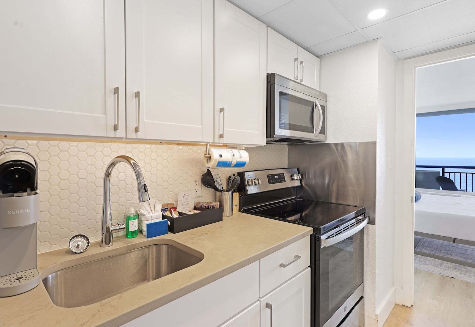 Modern kitchen with stainless steel appliances and ocean views from the bedroom beyond.