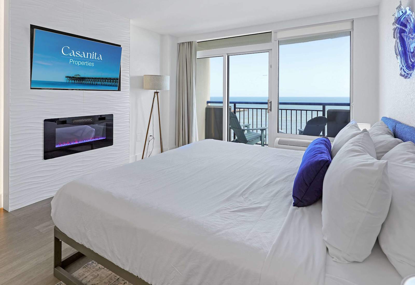 Relax in a bright Myrtle Beach studio with a cozy bed, wall-mounted TV, electric fireplace, and a comfortable coastal feel.