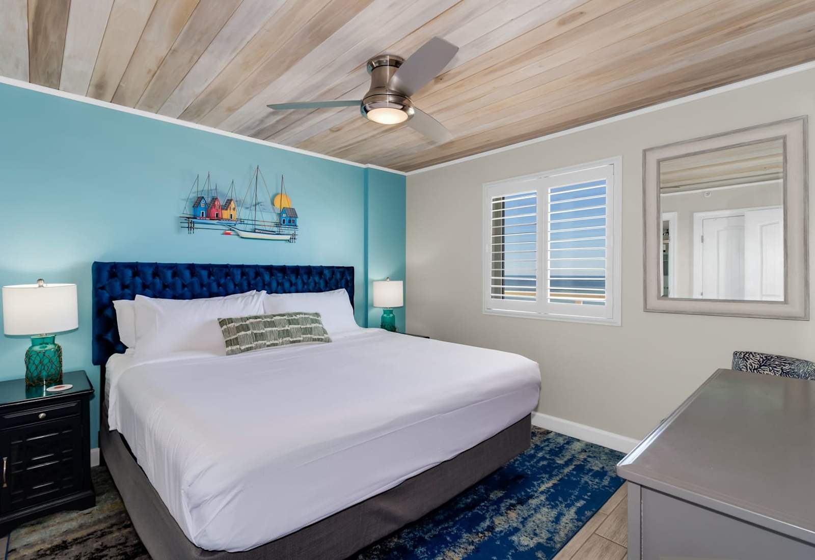 Unwind in this cozy bedroom featuring a plush king-sized bed, nautical-inspired decor, and a ceiling fan for added comfort. Wake up refreshed with natural light and glimpses of the ocean just outside your window—your perfect seaside retreat!