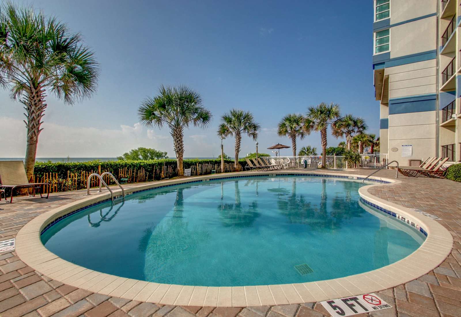 Outdoor resort pool surrounded by palm trees, lounge chairs, and coastal views for a refreshing break just steps from the beach.