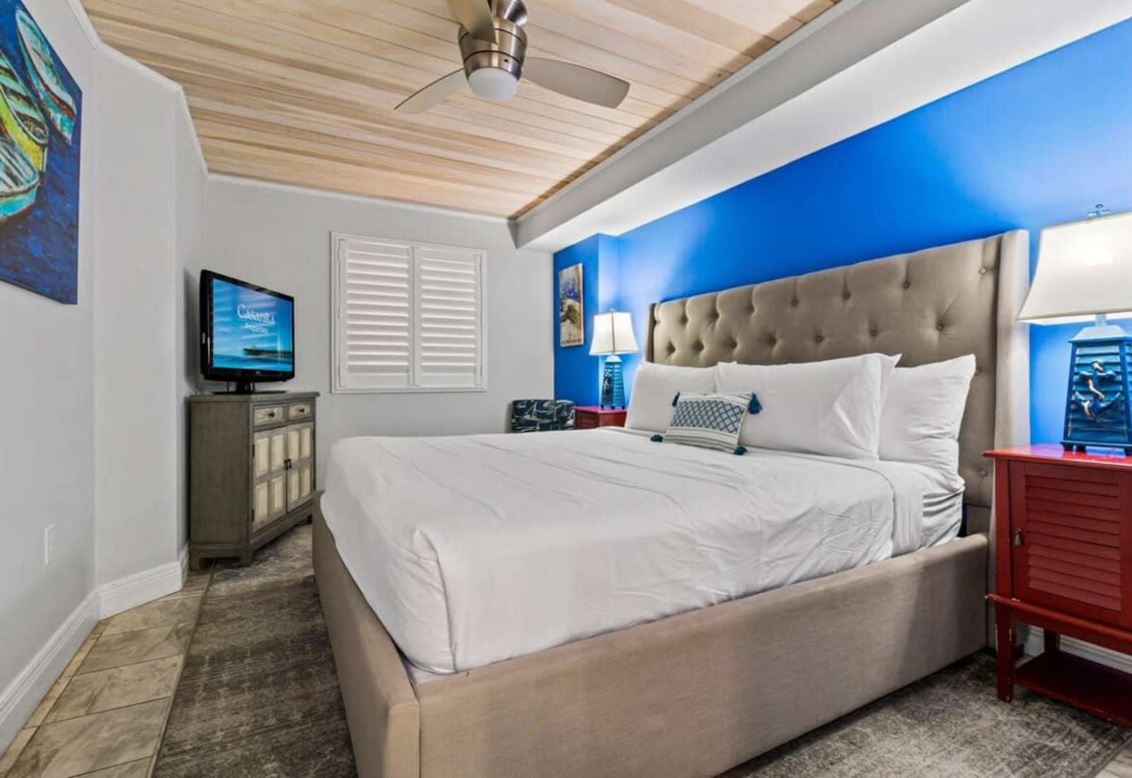 Unwind in this cozy bedroom featuring a plush king-sized bed, beach-inspired decor, and a ceiling fan for added comfort. 
