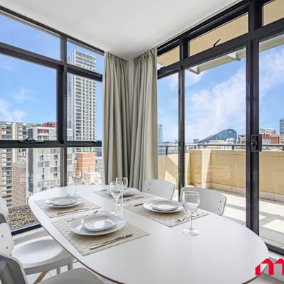 Dining area with table setting and floor-to-ceiling windows leading to the balcony with city views.