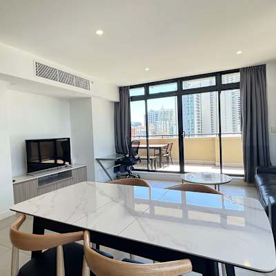 Open-plan living and dining area with sofa seating, TV, dining table, and balcony access.