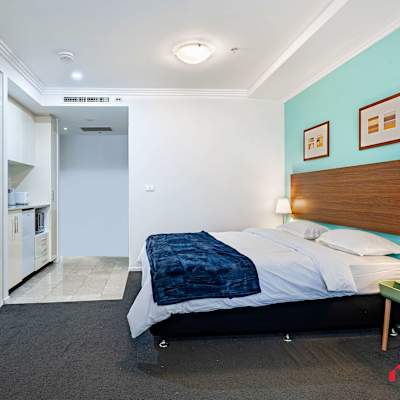 Bedroom featuring a comfortable king-size bed, bedside table with lamp, teal feature wall, and built-in wardrobe.