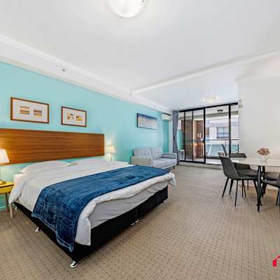 Spacious bedroom featuring a comfortable king-size bed, bedside tables with lamps, teal feature wall, and balcony access.