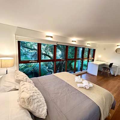 Bedroom featuring a queen-size bed, bedside tables, large windows, and leafy outlook.