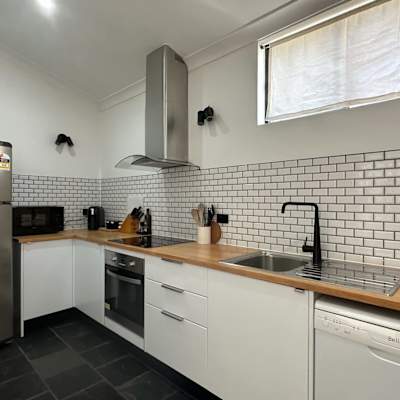Modern kitchen with stainless steel fridge, tiled splashback, cooktop, oven, and ample cabinetry.