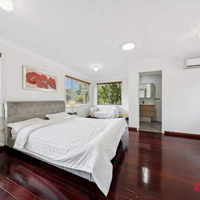 Bright bedroom featuring a comfortable queen-sized bed, large windows, air conditioning, and polished timber flooring.