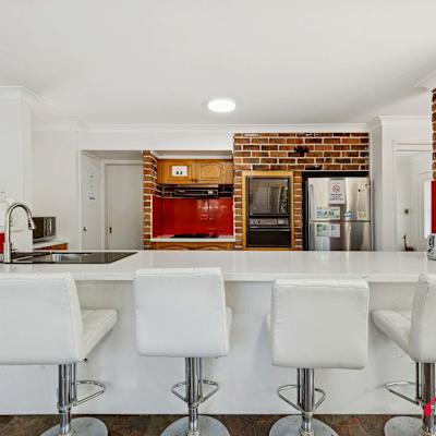 Contemporary kitchen with island bench, white bar stools, and brick feature wall.