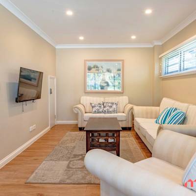 Living area with sofa, wall-mounted TV, staircase, and neutral décor.