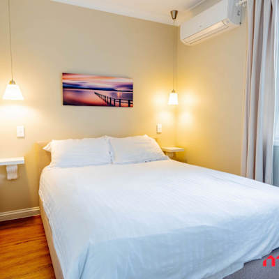 Bedroom with a queen-sized bed, bedside lamps, wall artwork, and air conditioning.