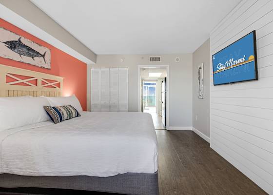Rest easy in this vibrant and spacious bedroom featuring a plush bed, cozy coastal decor, and artistic wall accents that capture the essence of a beach getaway. With comfort and style in every detail, it’s the perfect space for a peaceful retreat