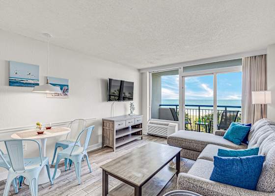 Oceanfront comfort meets modern style — unwind in this bright, coastal living space featuring panoramic beach views, a cozy sectional, and a private balcony perfect for morning coffee or sunset relaxation.