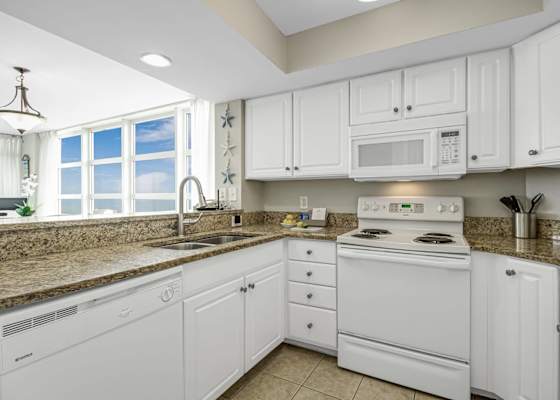 Bright kitchen with granite countertops, white cabinetry, full-size appliances, and ocean views flowing in from the nearby living area.