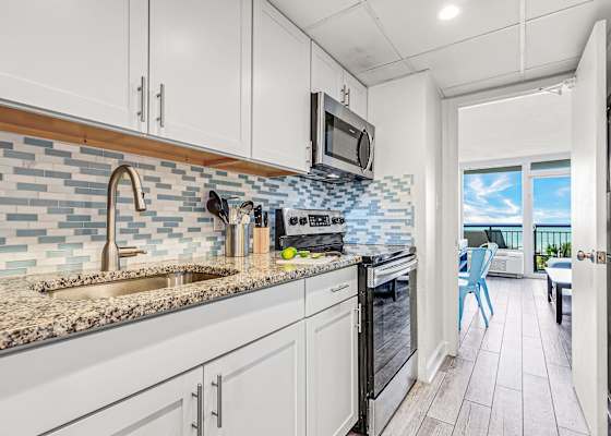 Modern kitchen with sleek cabinetry and a stylish blue-tile backsplash, fully equipped for your culinary needs. Just steps from the bedroom, this space offers convenience and functionality, allowing you to enjoy meals with a stunning ocean view.