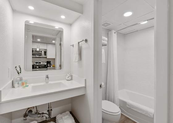 A bright, modern bathroom with crisp white tiles, a relaxing bathtub, and plush towels awaits your stay! 
