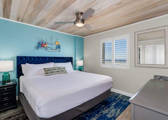 Unwind in this cozy bedroom featuring a plush king-sized bed, nautical-inspired decor, and a ceiling fan for added comfort. Wake up refreshed with natural light and glimpses of the ocean just outside your window—your perfect seaside retreat!