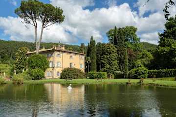 Large lake with a swan on in front of a cream villa