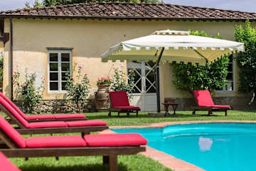 Red sun beds around a pool in front of a cream house