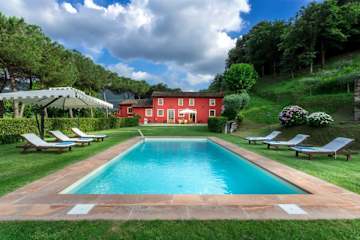 Red house behind a swimming pool surrounded by grass