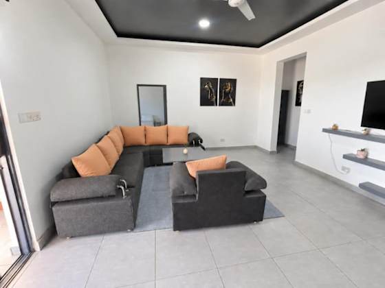 A wide view of the living room’s corner sofa, orange cushions and television.