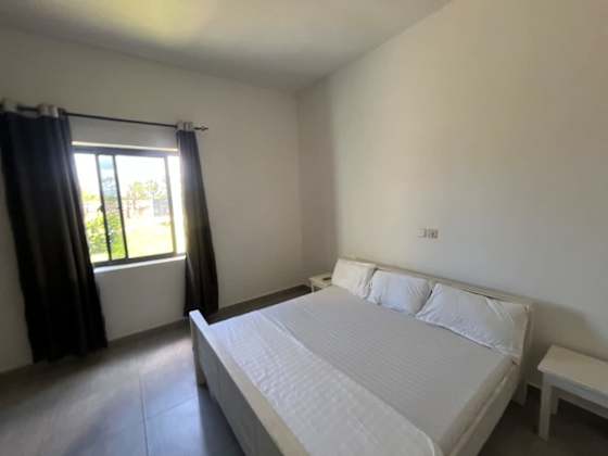 A light-filled bedroom with white bedding and dark curtains.