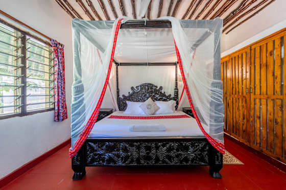 A net-draped bed and carved wooden furniture in one of Baraza’s two enclosed bedrooms.