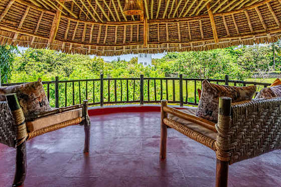 The upstairs balcony offers wicker seating and a leafy outlook beneath the thatched roof.