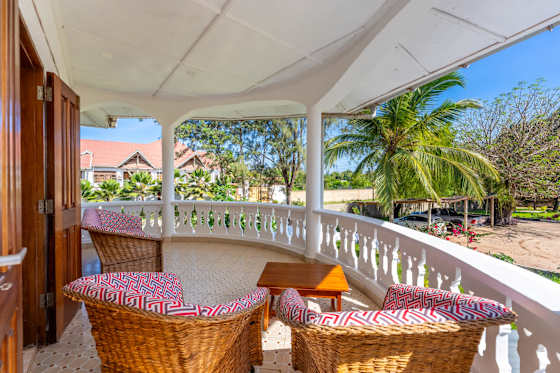 A covered balcony with wicker seating, a table and views over the greenery.