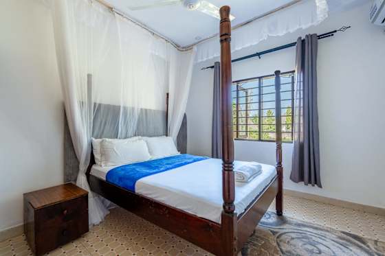 A wooden four-poster bed with mosquito netting and a blue bed runner.