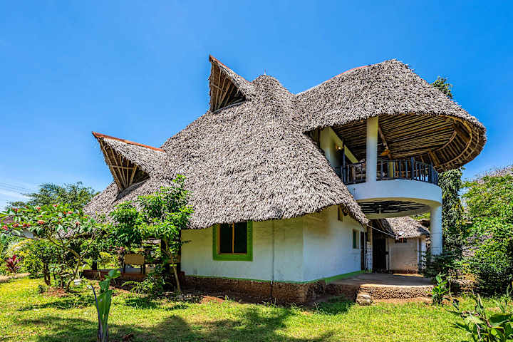 Villa Baraza’s sweeping makuti roof and green shutters, framed by its tropical garden.