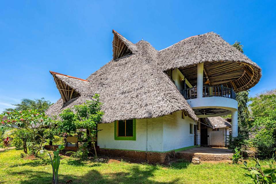 Villa Baraza’s sweeping makuti roof and green shutters, framed by its tropical garden.