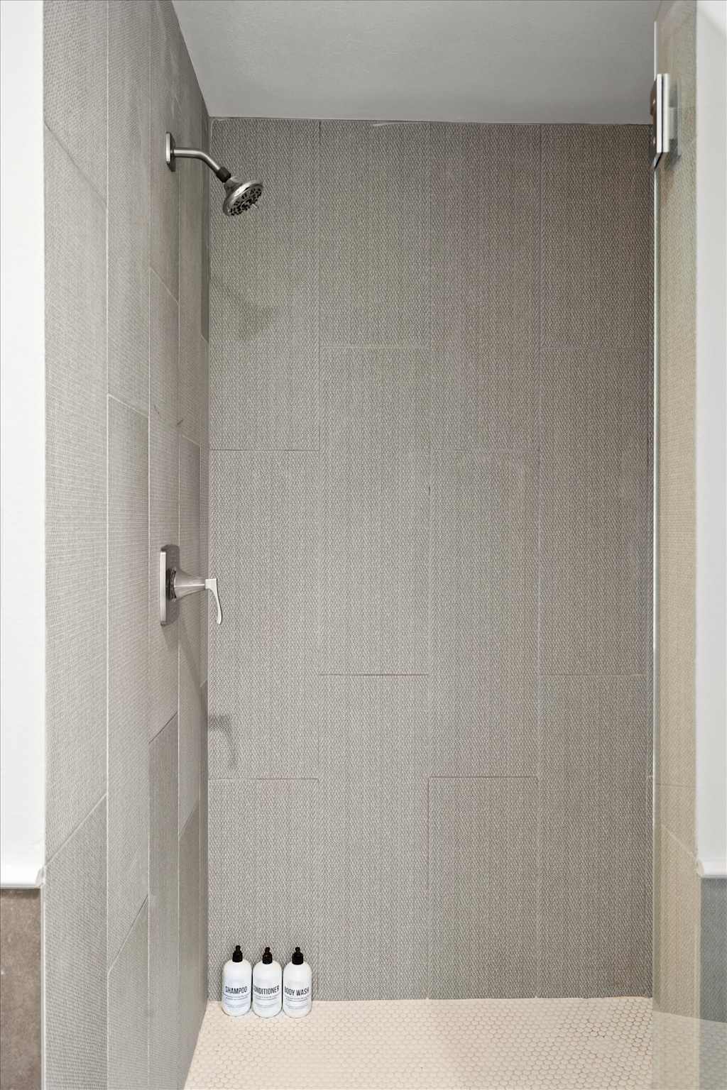The Sunkiss — walk-in shower with textured grey tiles, chrome fixtures, and toiletry bottles