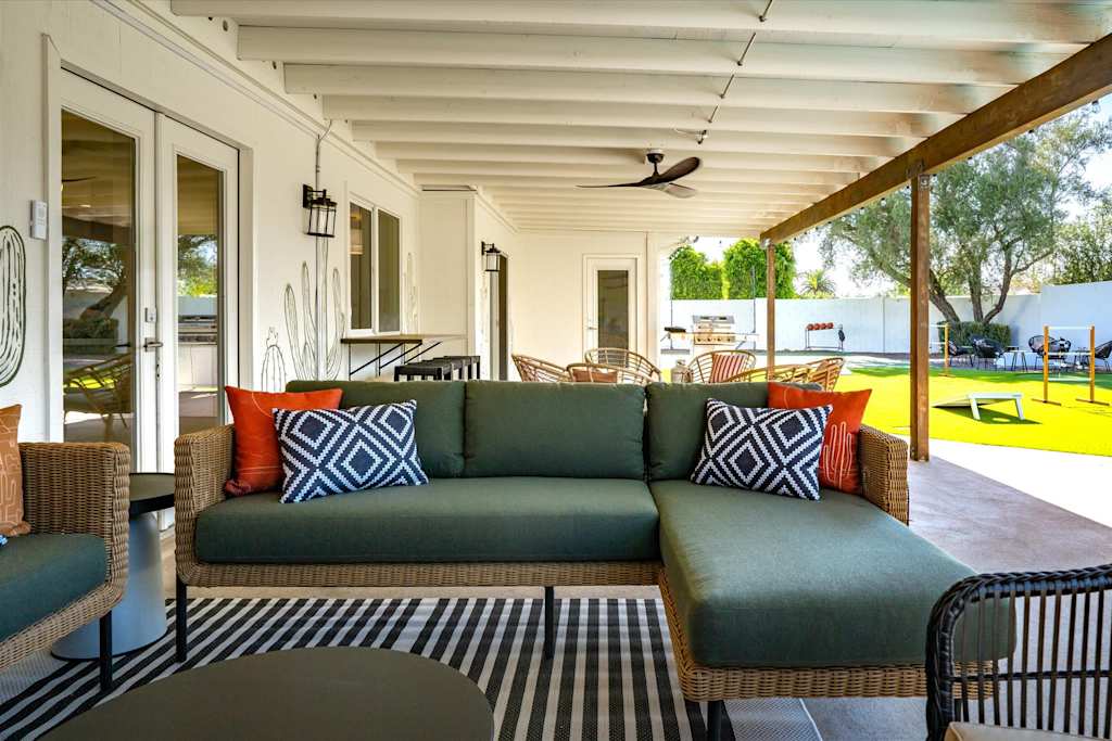The Sunkiss — covered patio with a green sectional sofa, accent pillows, striped rug, and ceiling fan