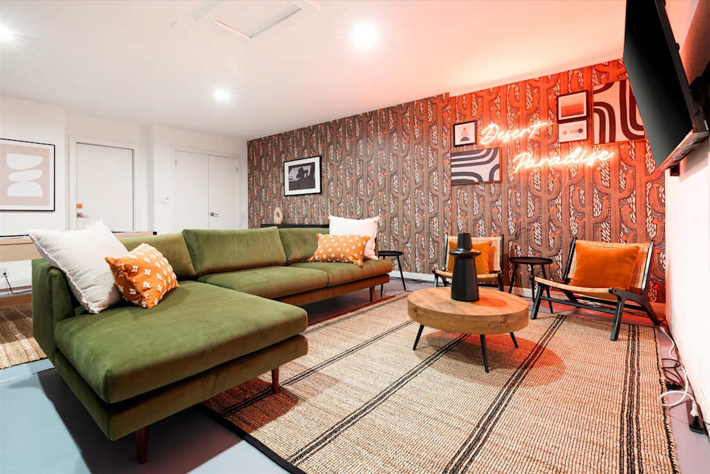 The Sunkiss — living room with green sectional sofa, round coffee table, accent chairs, and patterned wallpaper with neon sign