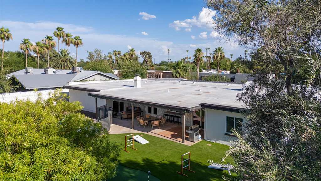 The Sunkiss — aerial view of a home backyard featuring artificial turf, lawn games, covered patio, and palm trees