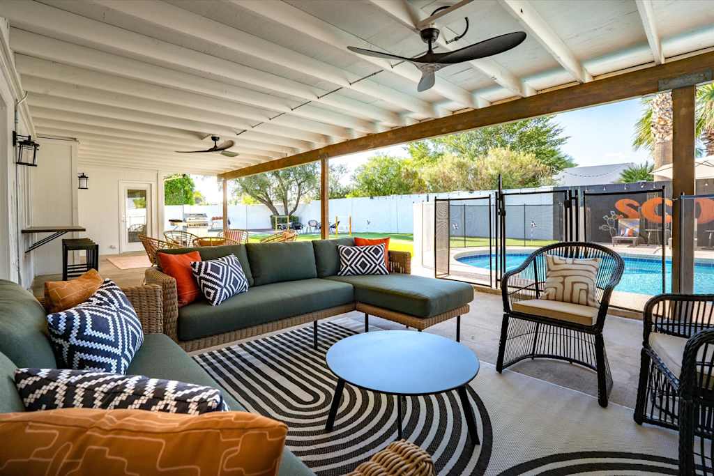 The Sunkiss — covered patio with outdoor sectional sofa, armchairs, ceiling fans, and a view of the fenced pool