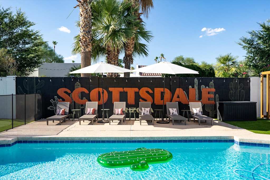 The Sunkiss — swimming pool with cactus float, row of sun loungers, umbrellas, and painted wall under palm trees