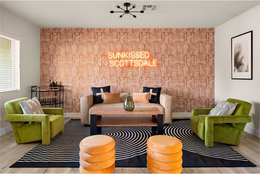 The Sunkiss — sitting area with couch, green armchairs, round orange stools, patterned wallpaper, and neon sign