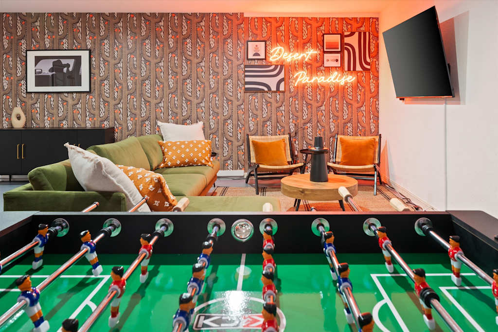 The Sunkiss — foosball table in the foreground of a game room with green sofa and neon sign