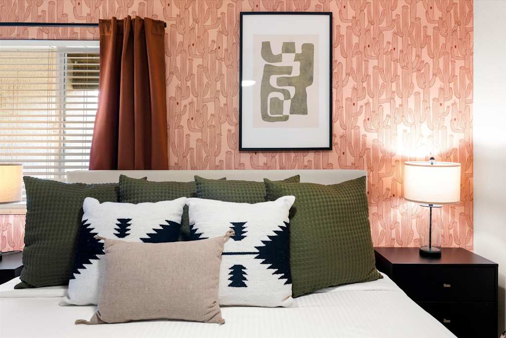 The Sunkiss — bed with accent pillows in front of pink cactus-patterned wallpaper and framed artwork