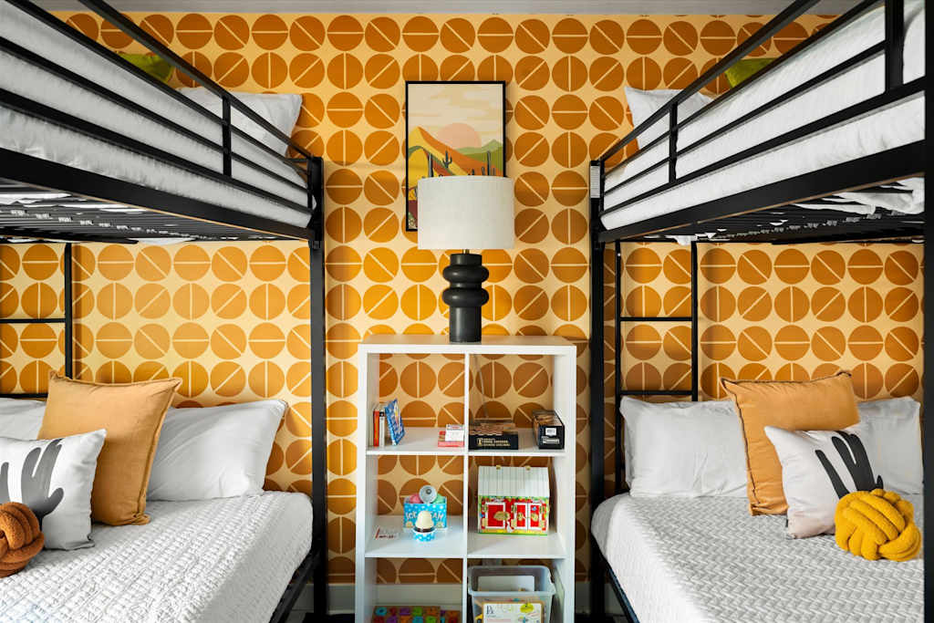 The Sunkiss — bunk room with two metal bunk beds, yellow geometric wallpaper, and a central shelving unit