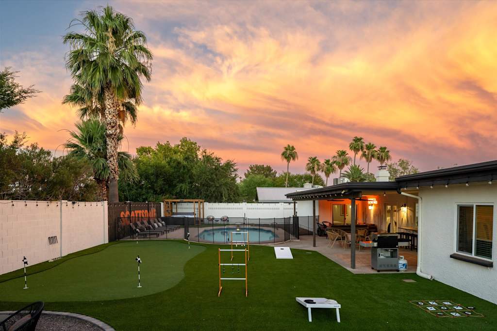 The Sunkiss — spacious backyard at sunset featuring a putting green, lawn games, pool, and covered patio
