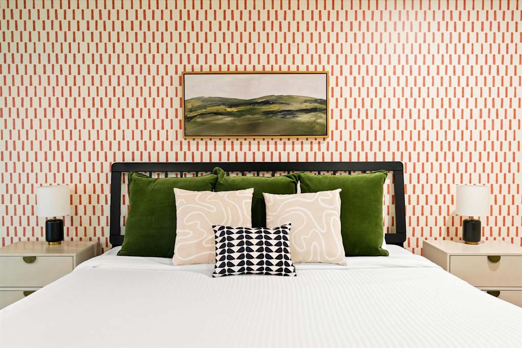 The Sunkiss — bedroom with geometric wallpaper, black headboard, decorative green pillows, and nightstands with lamps