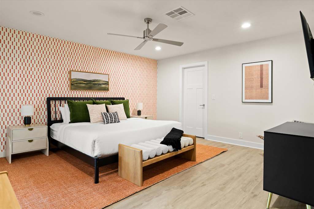The Sunkiss — spacious bedroom with patterned wallpaper, black bed, wooden bench, orange rug, and wall-mounted tv